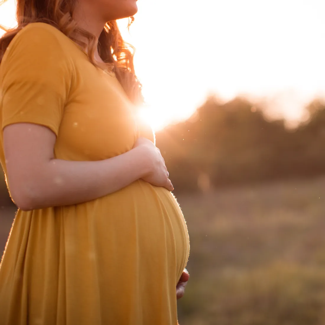 Schwangere Frau hält ihren Babybauch im Abendlicht